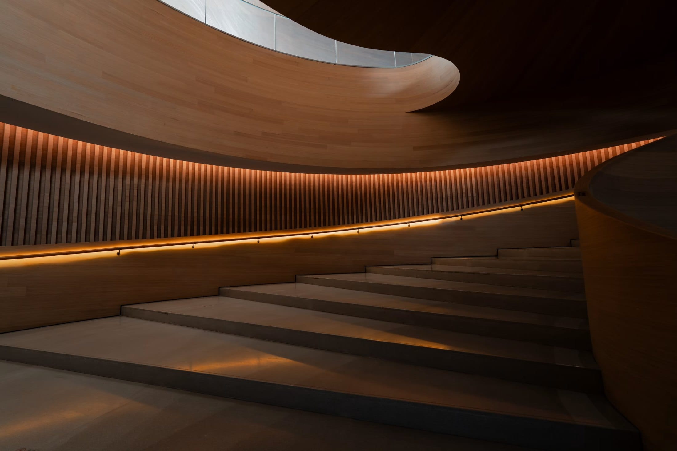 Curved timber stair with concealed architectural cove lighting and an illuminated handrail
